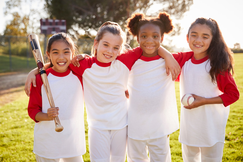 Group of girls wearing uniforms while holding baseball gear